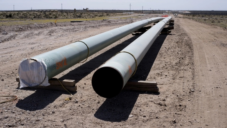 Steel pipeline segments laid along an unpaved construction corridor